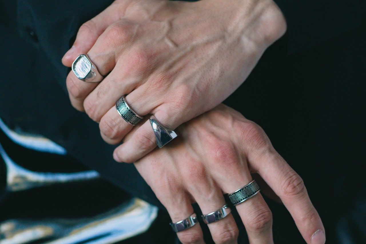 a pair of hands wearing six silver, chunky fashion rings