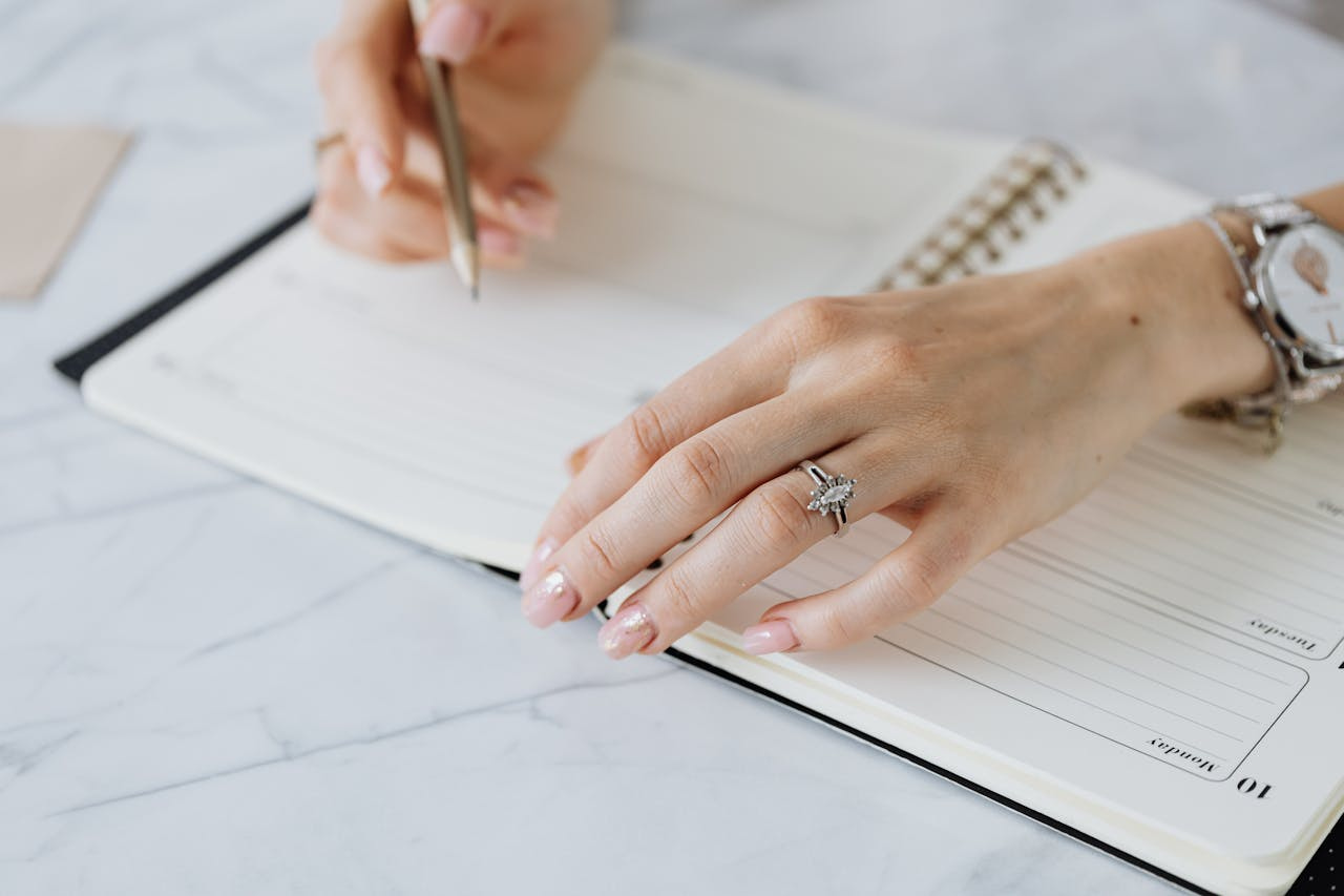 A woman writing in a planner, a marquise cut engagement ring on her finger.