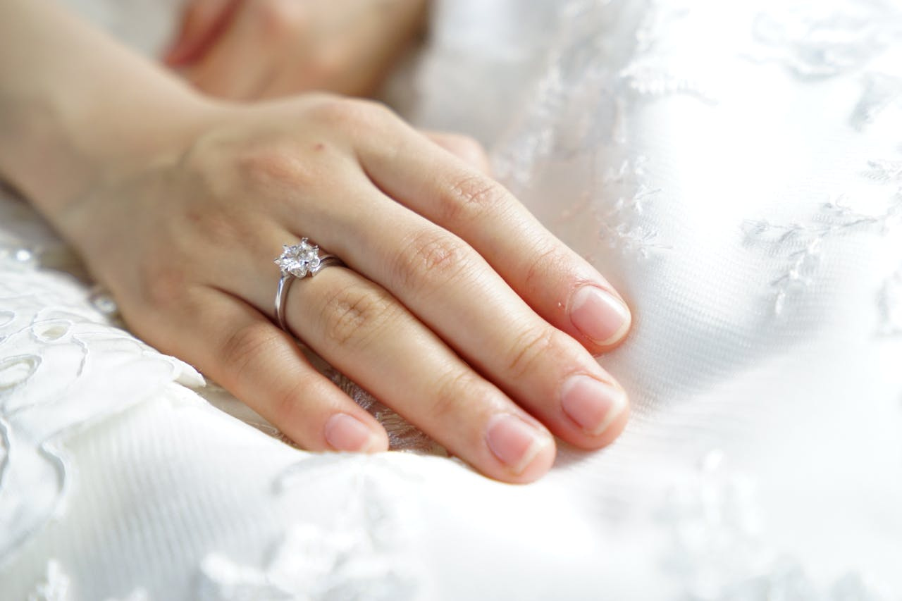A woman resting her hand in her lap while wearing her wedding dress, a sparkling engagement ring on her finger.