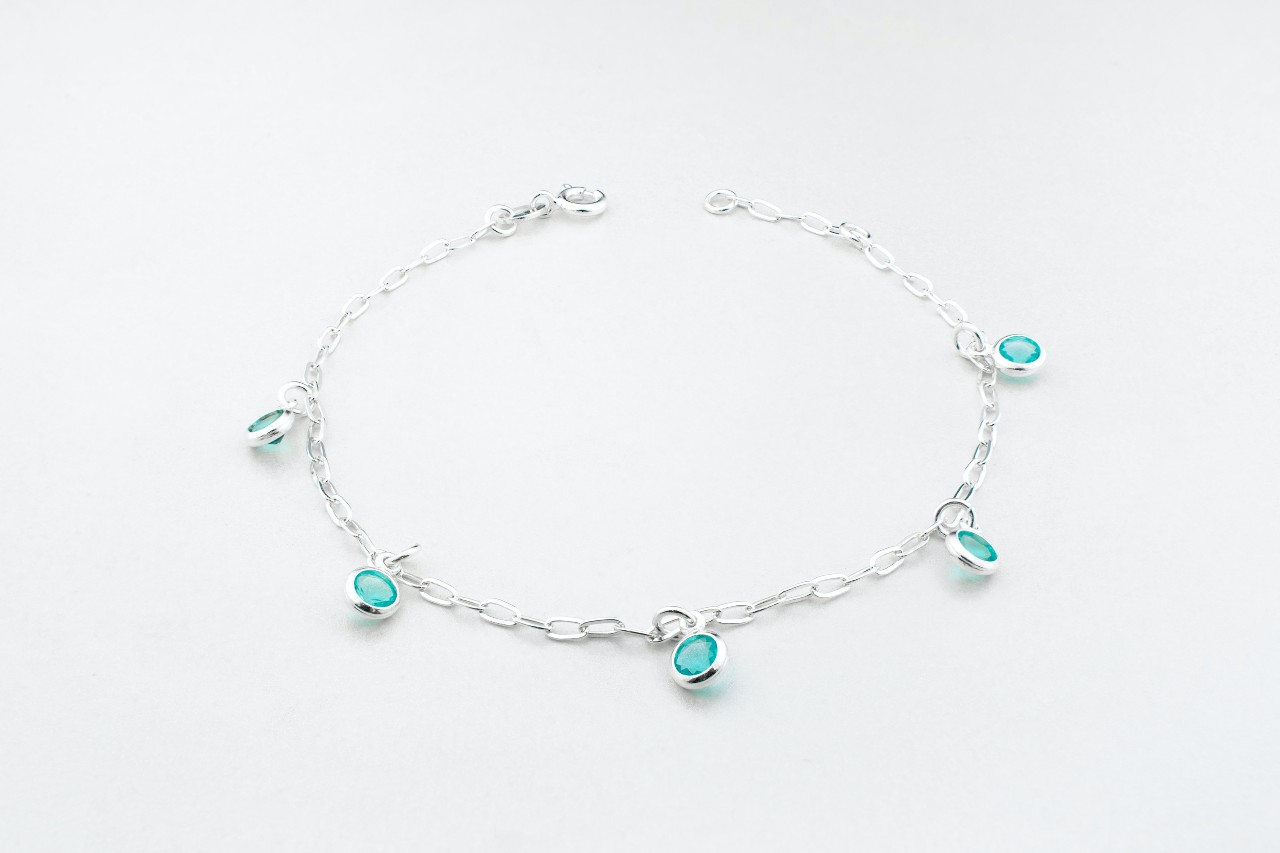 A silver chain bracelet adorned with small aquamarine charms on a white background