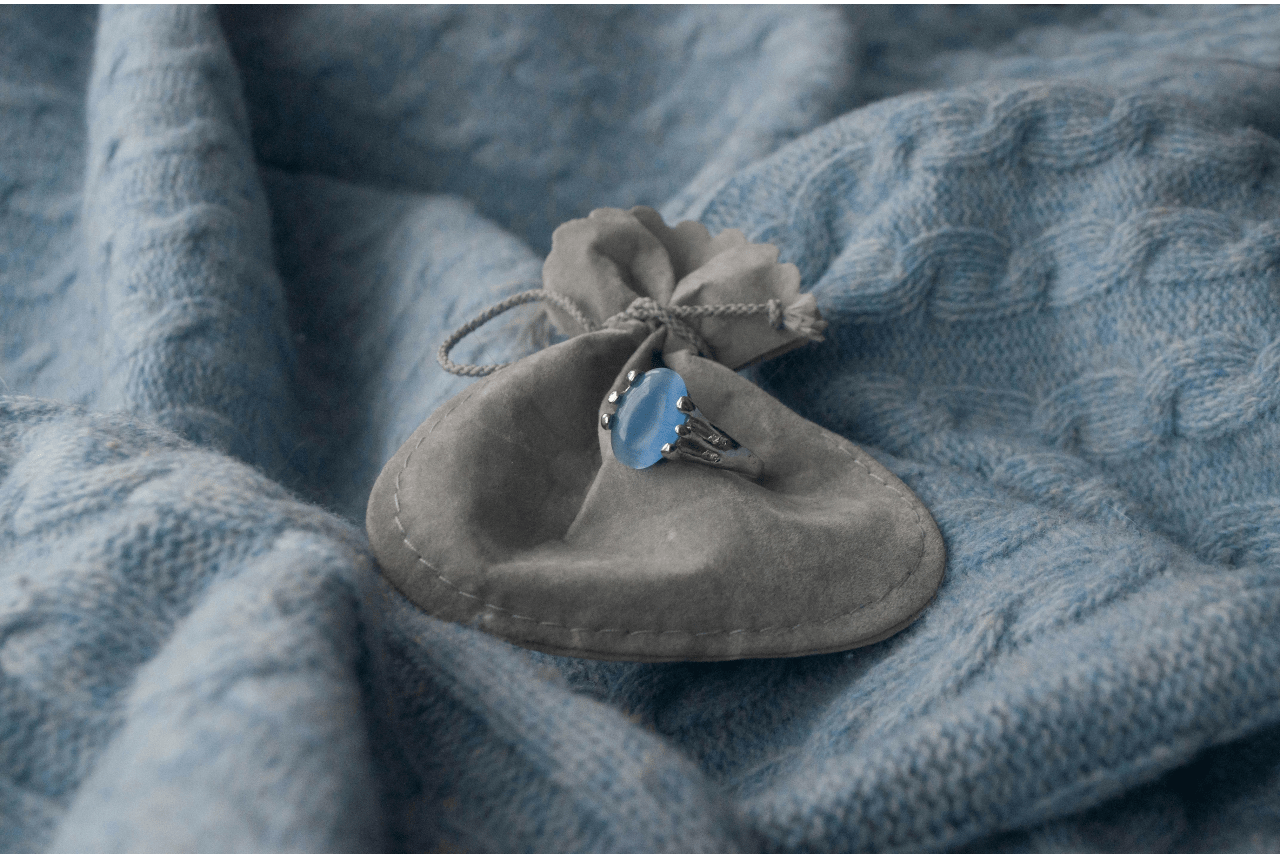 a silver fashion ring with an oval cut aquamarine sitting on a gray bag