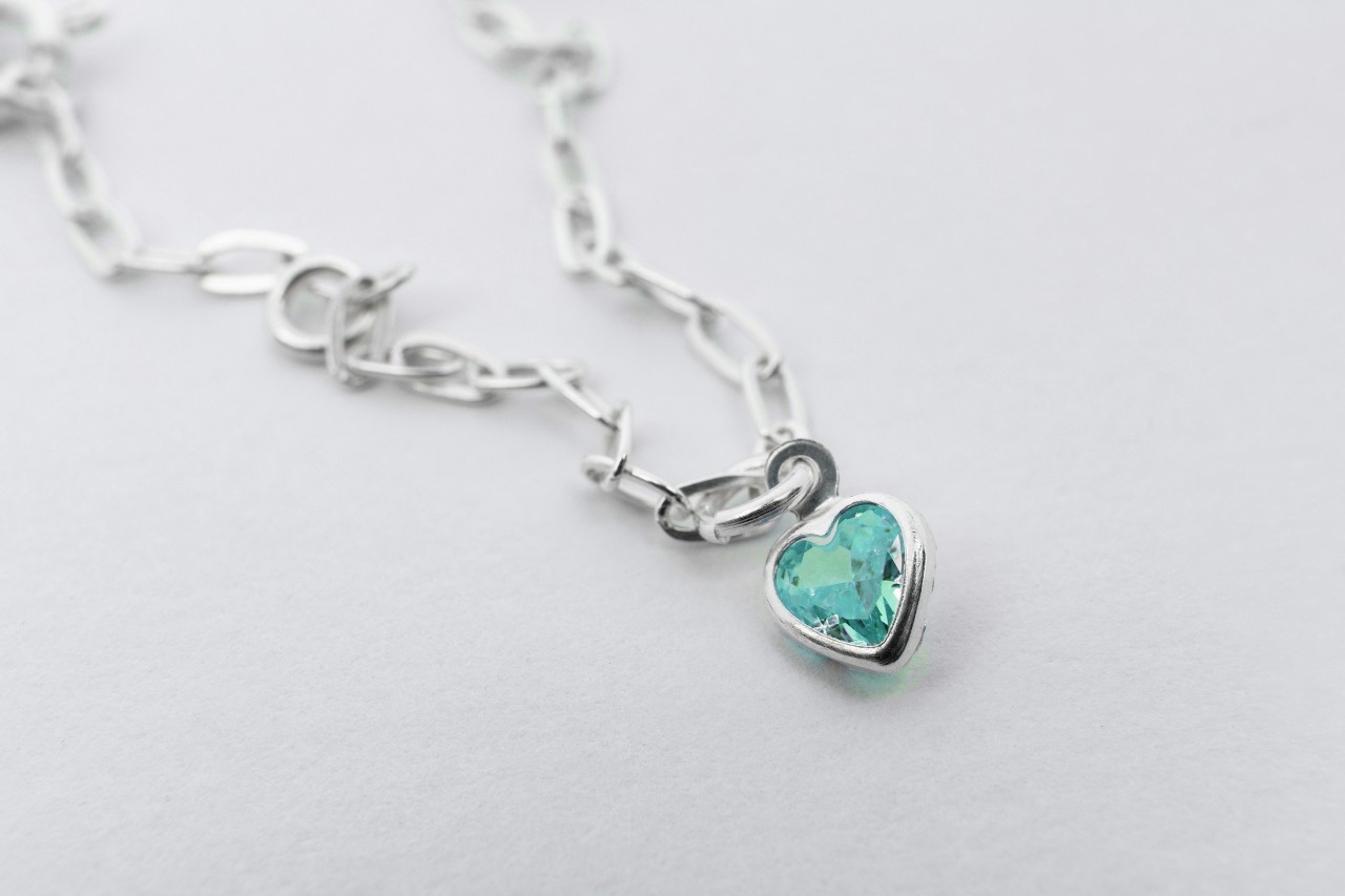A silver chain necklace with heart shaped aquamarine pendant on a white surface