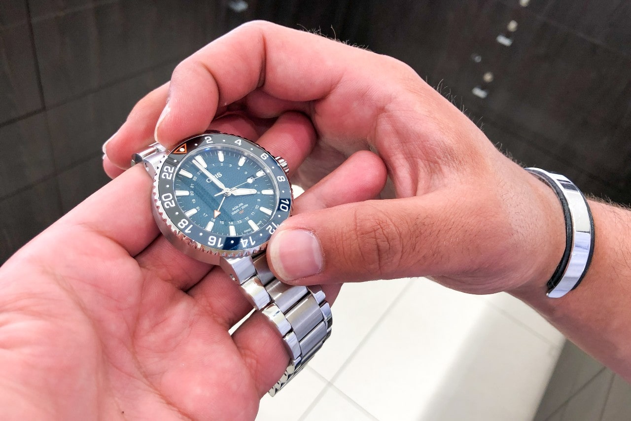 A close-up of a man holding a metallic Oris watch with a deep blue dial