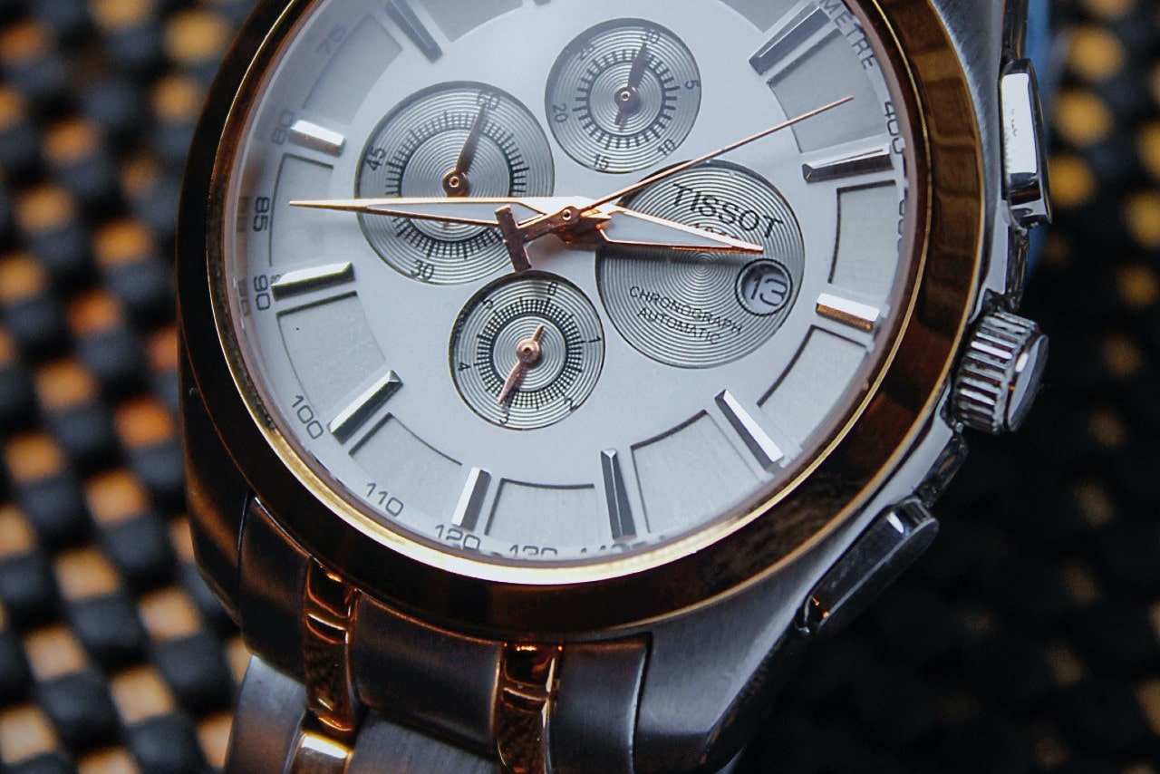 A close-up of a white and rose gold metallic TISSOT watch with several complications inside the white dial