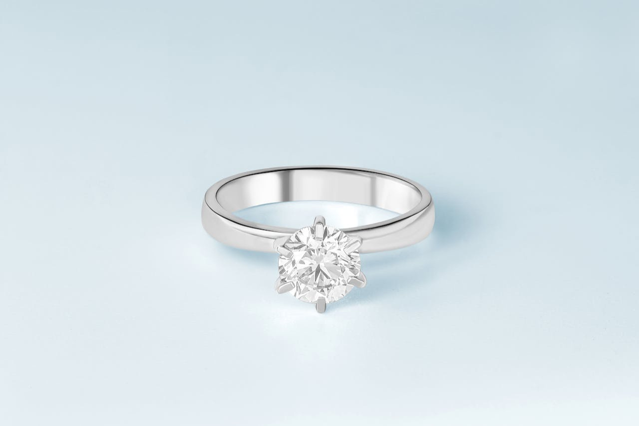 A white gold solitaire diamond engagement ring on a blue surface.