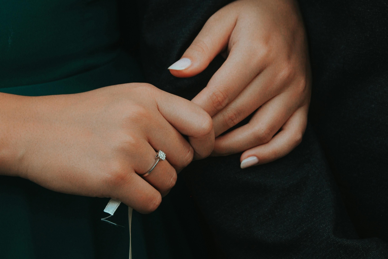 A close up of a white gold diamond engagement ring on a woman’s hand with white manicure.