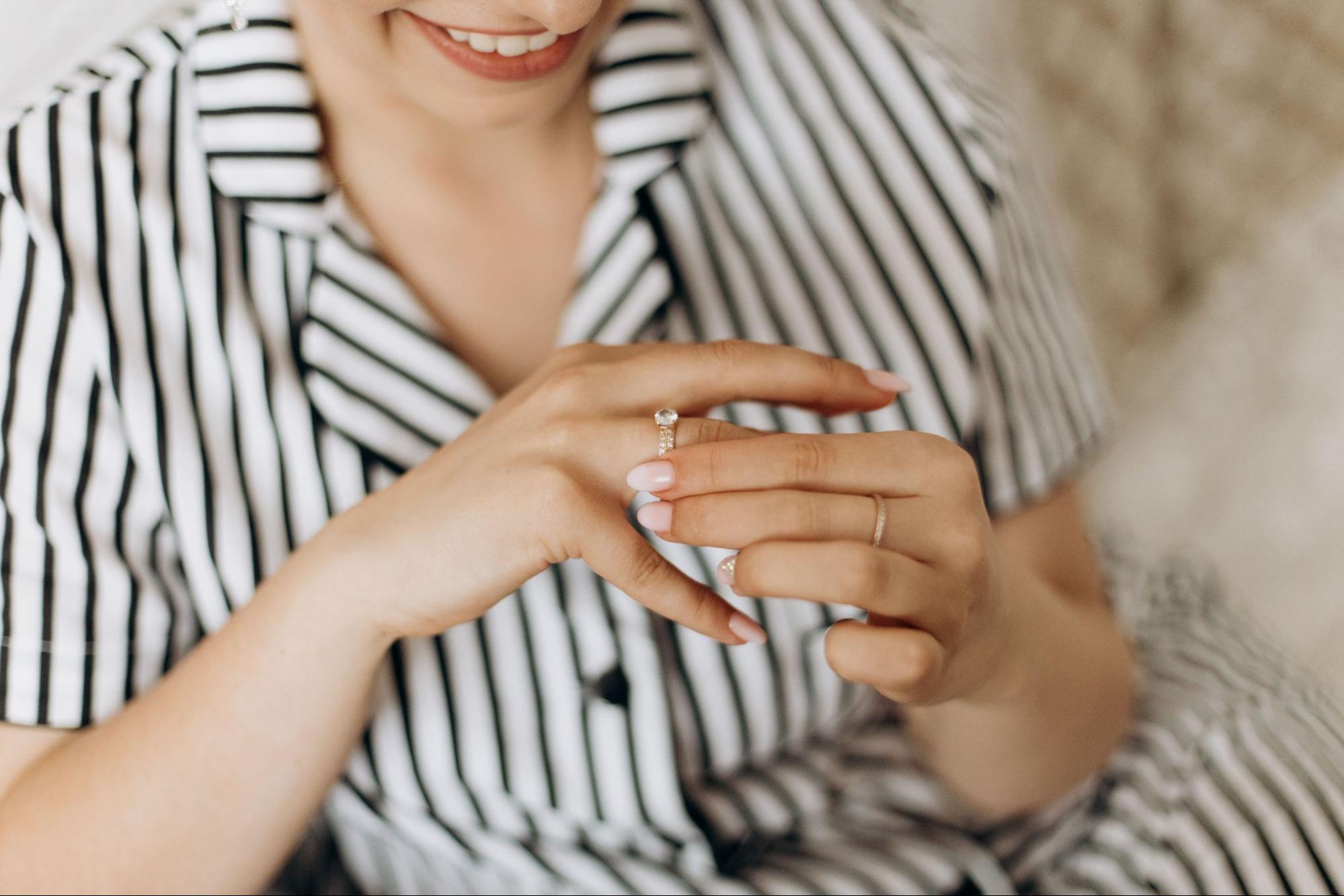 A woman in a striped shirt smiles while trying a diamond ring on her finger.