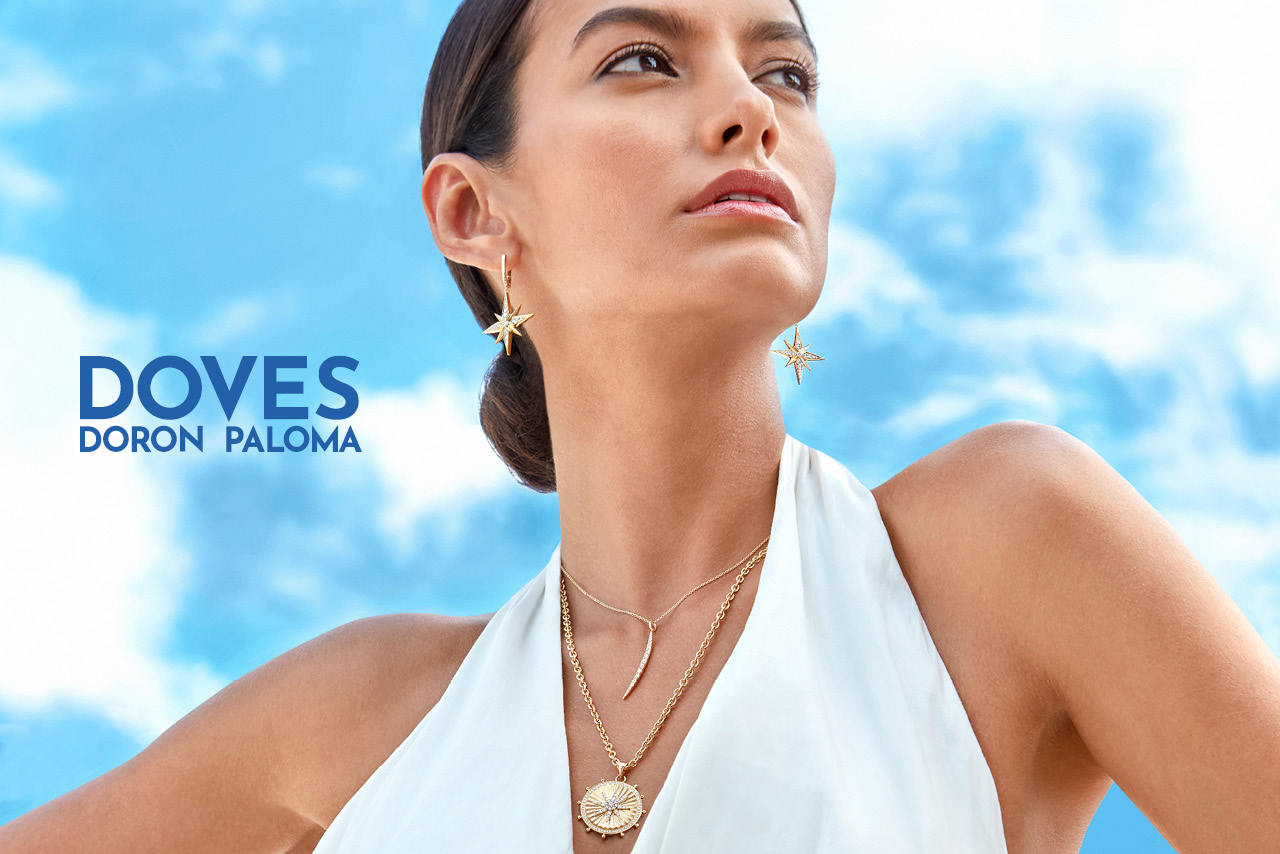 Fashionable woman wearing attractive Doves by Doron Paloma earrings and necklaces looks off into the distance against a cloudy sky