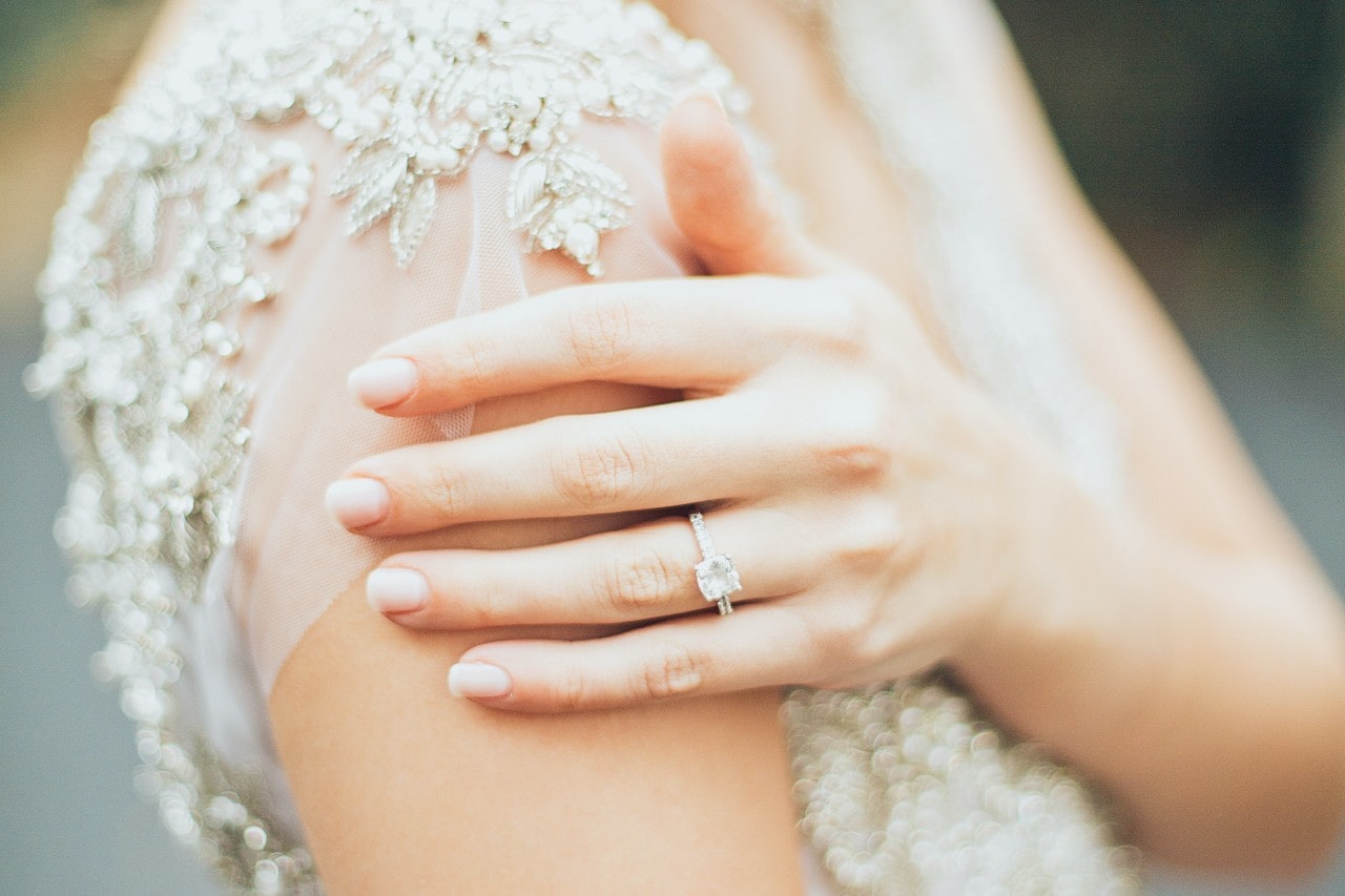a bride resting her hand on her arm, wearing a white gold side stone engagement ring