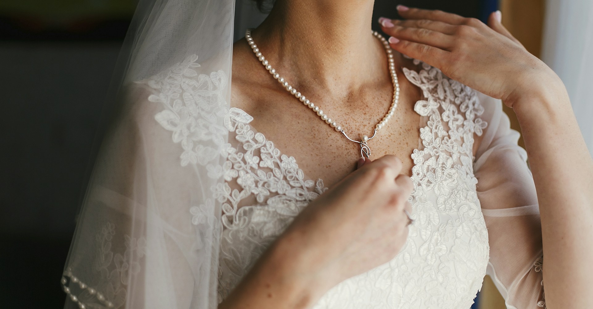 A bride wearing a delicate single-strand pearl necklace with a silver drop pendant.