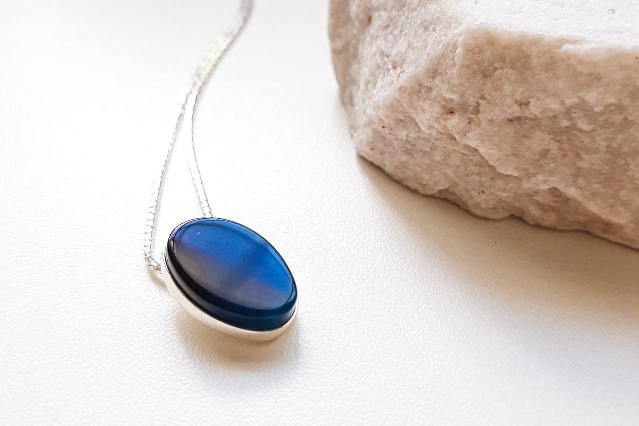 a white gold pendant necklace featuring a blue oval stone on a white surface