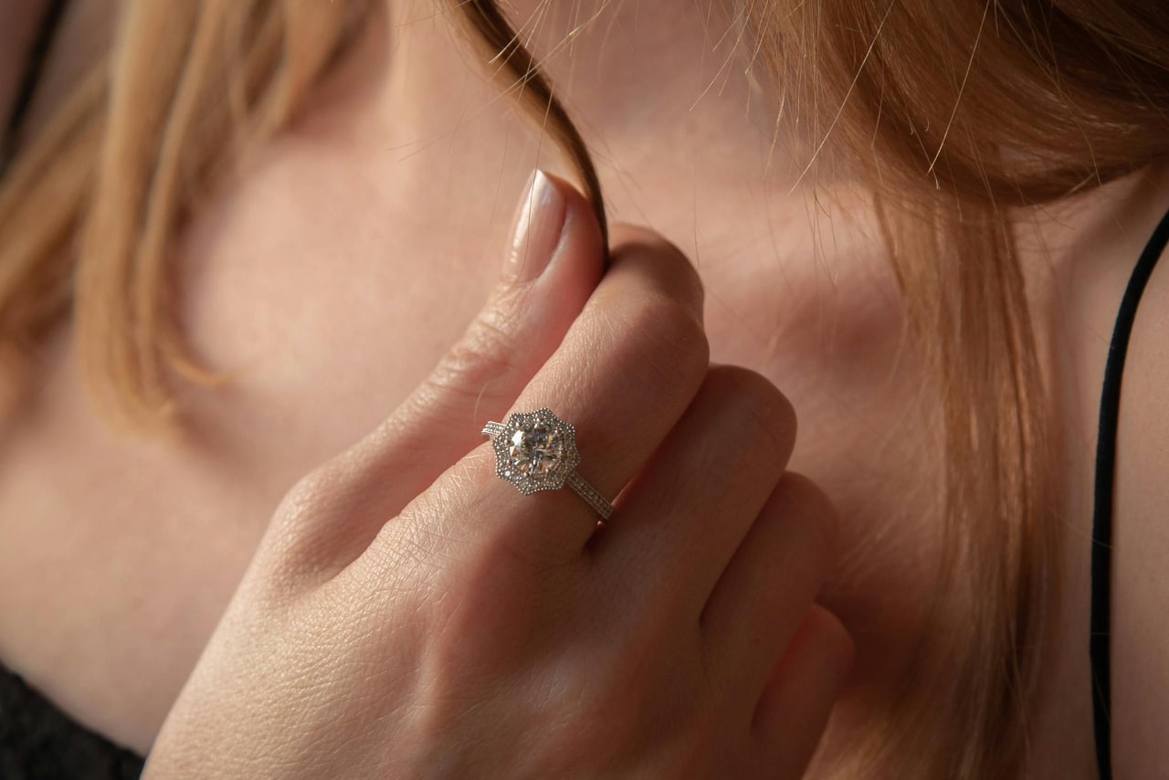 A woman holding a strand of her red hair and showcasing a beautiful diamond halo engagement ring.