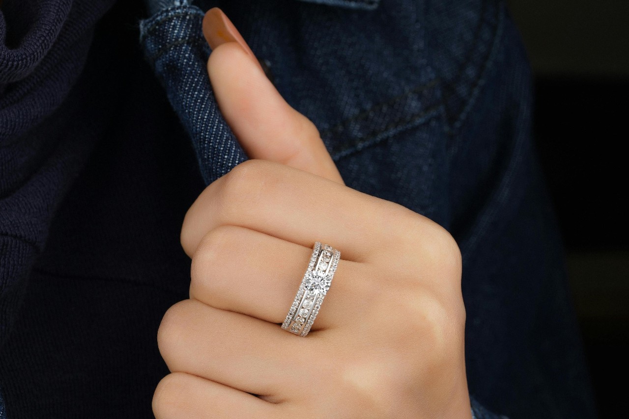 A close-up of a hand wearing an elegant diamond-studded ring, set against a dark denim jacket.