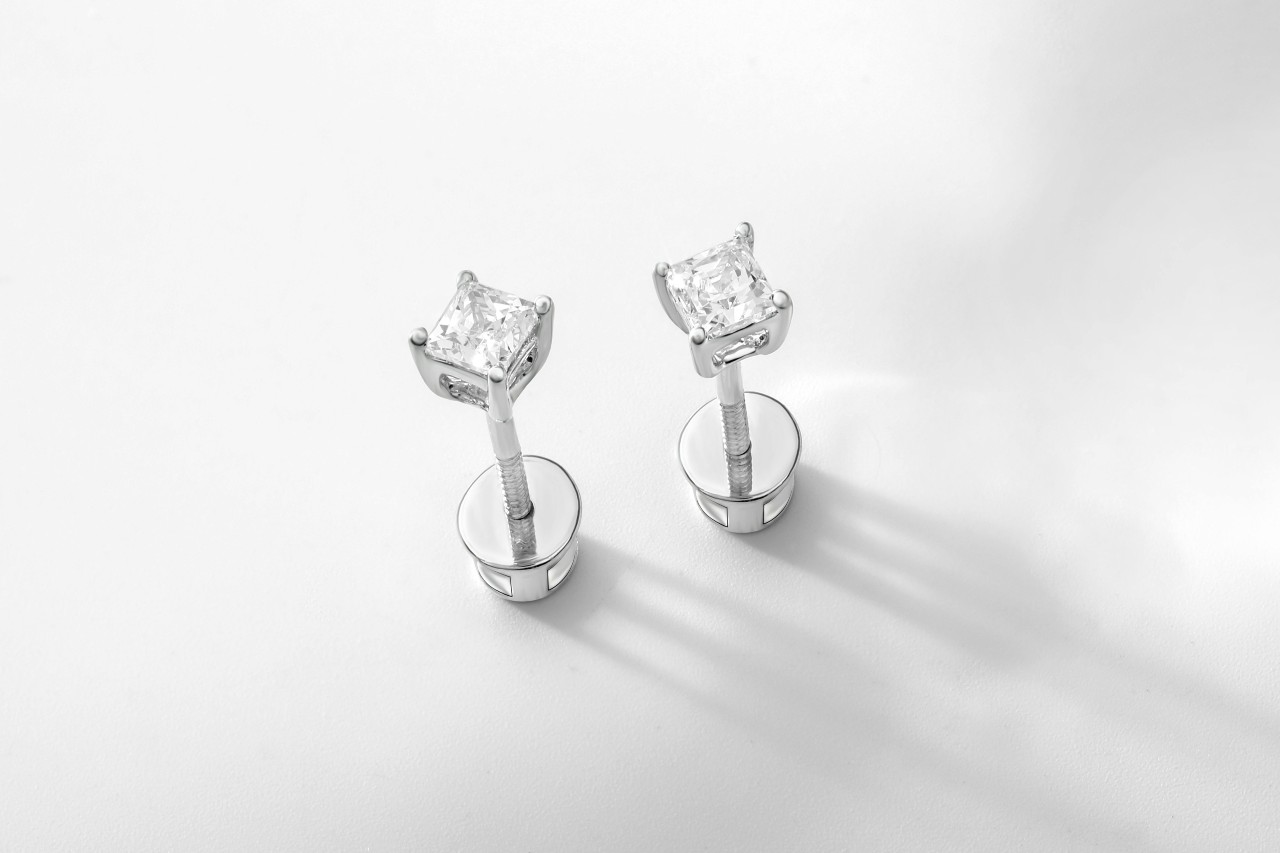 A close-up of a princess cut white gold diamond studs on a white background