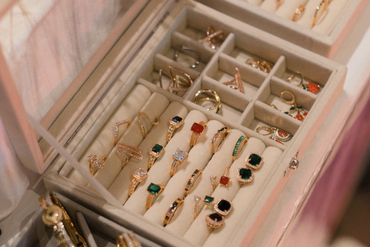 A neatly organized jewelry box displays an assortment of gold rings with colorful gemstones.