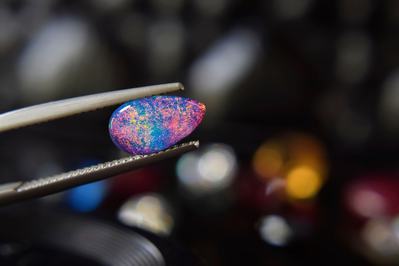 A close-up of a purple and blue multicolor stone being held with a pair of pliers.