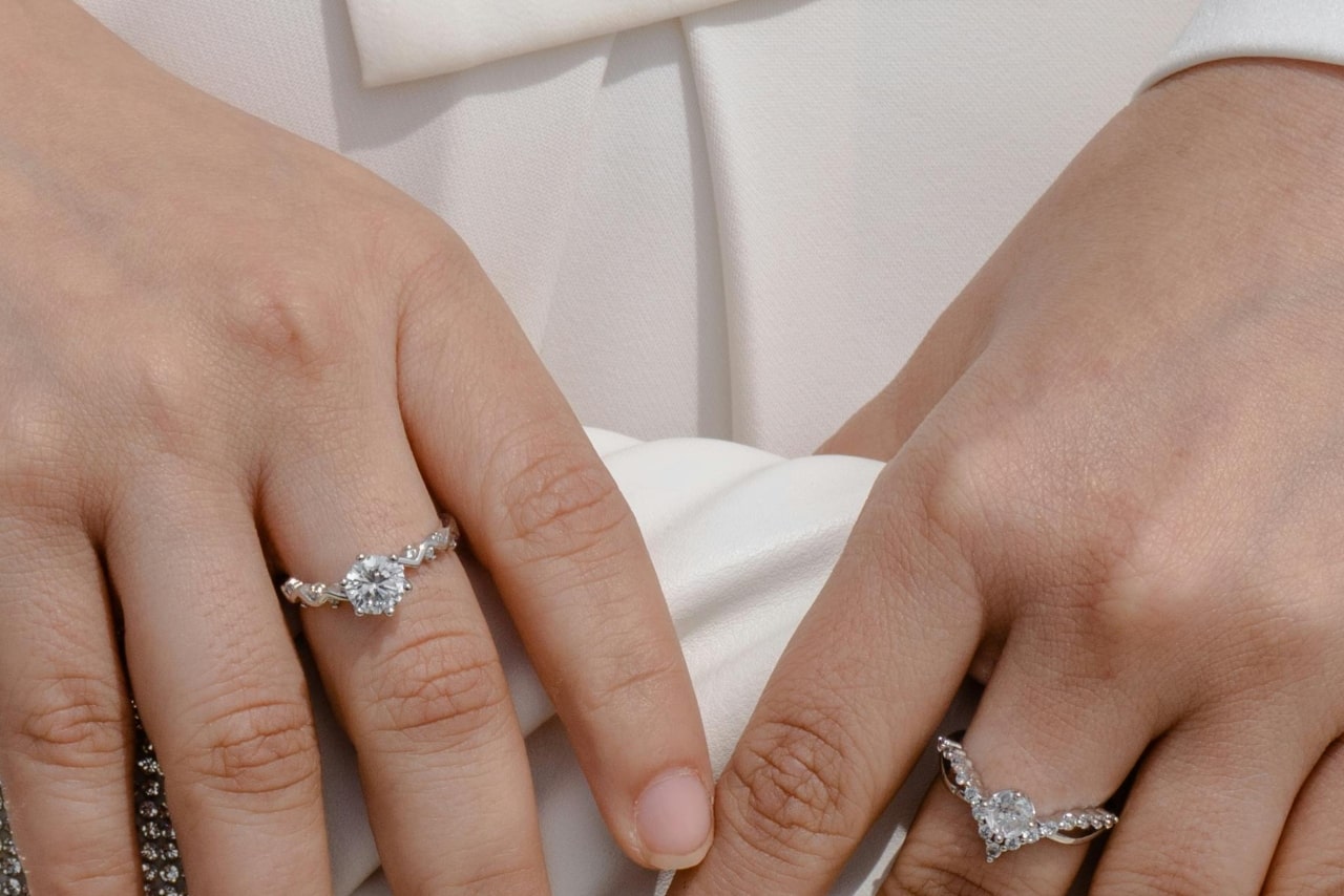 A close-up of someone holding a white clutch, showcasing two beautiful diamond rings, one on each hand.