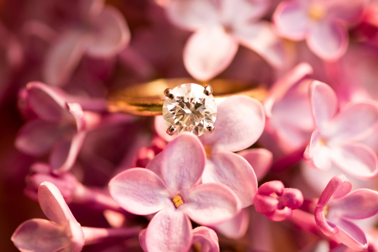 A golden engagement ring tucked in a group of pink flowers.