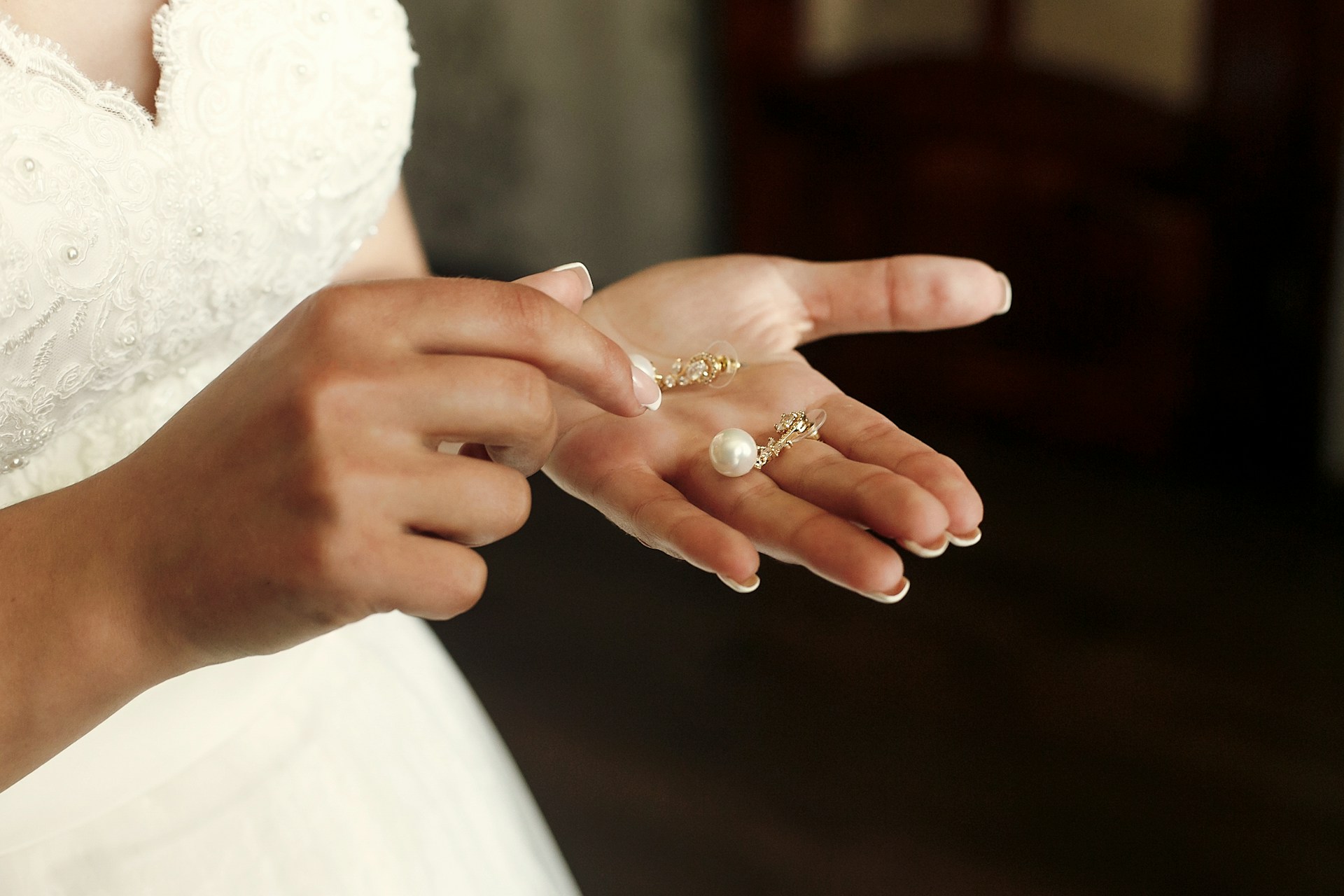 A close up of a drop pearl earrings on a bride’s palm.