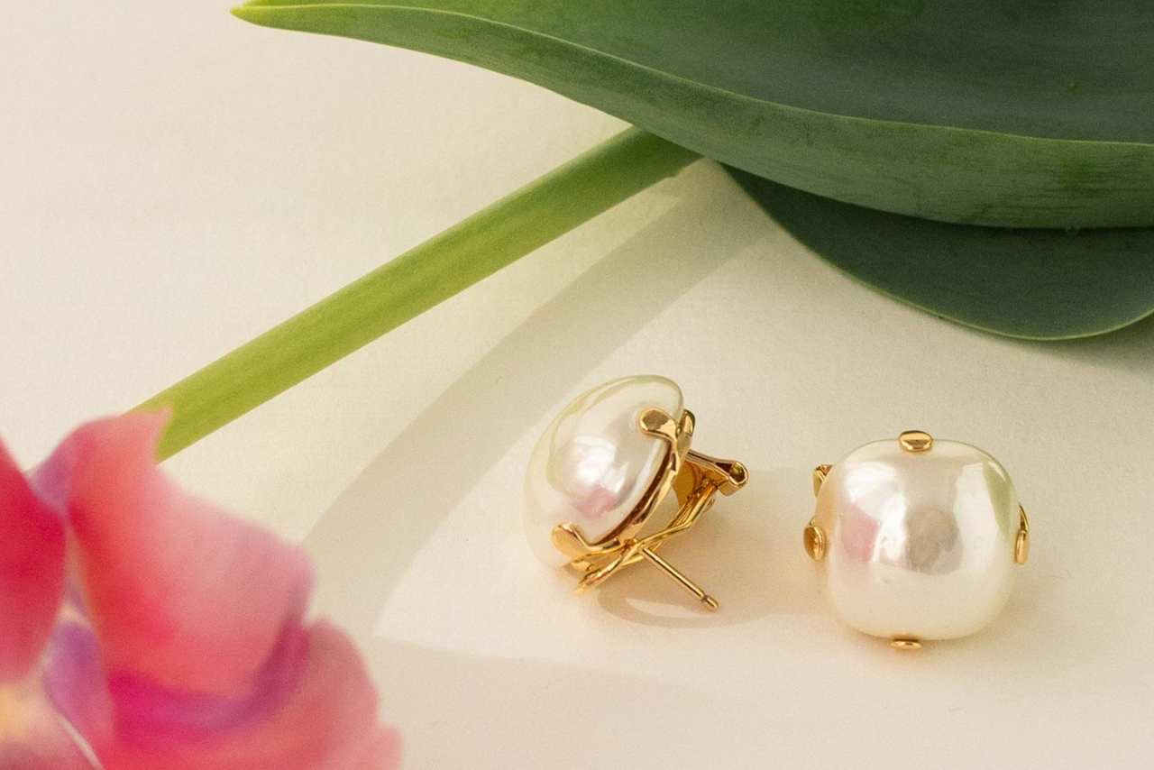 Yellow gold pearl stud earrings on a white surface near the tulip.