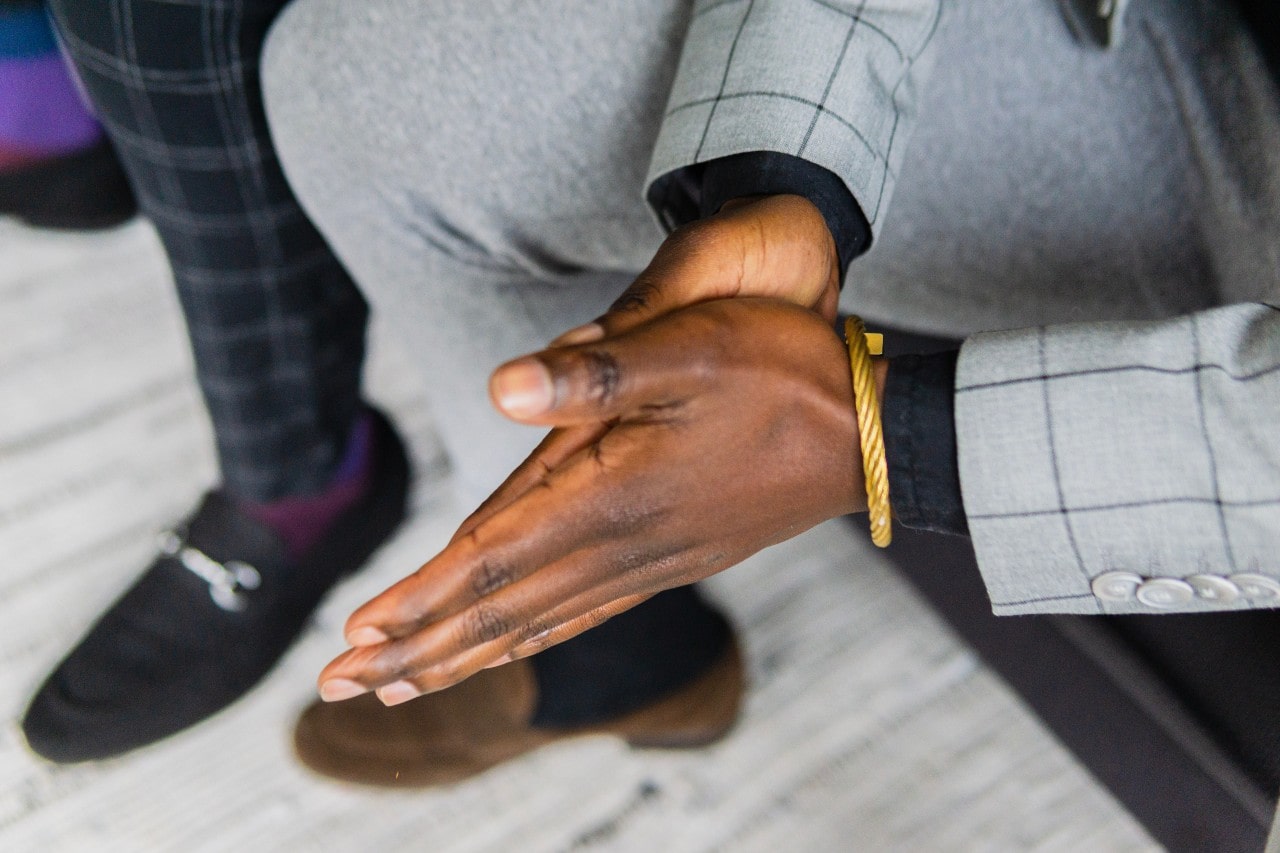 A close-up of a man holding his hands flat to each other, showcasing his golden rope-twisted bracelet.