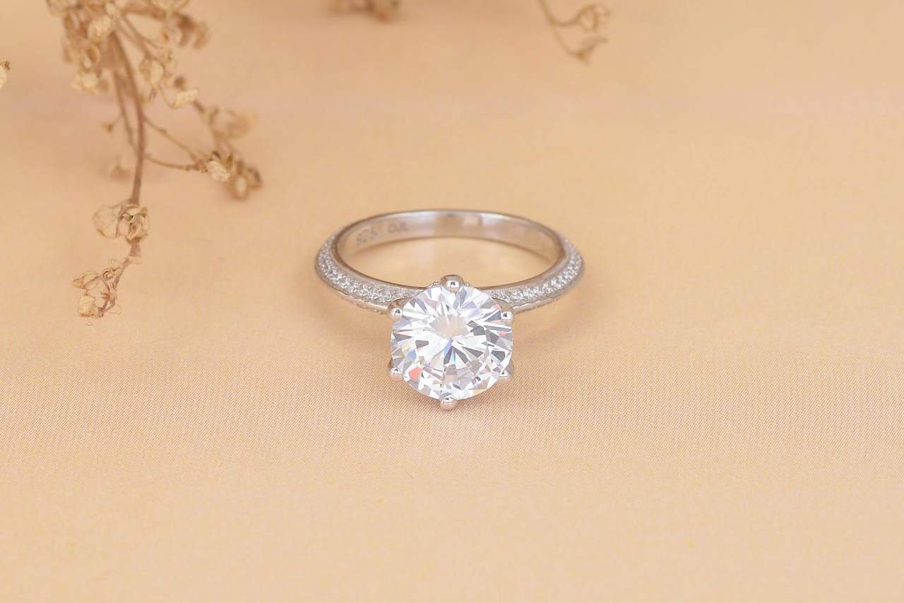 A side stone diamond engagement ring on a beige surface.