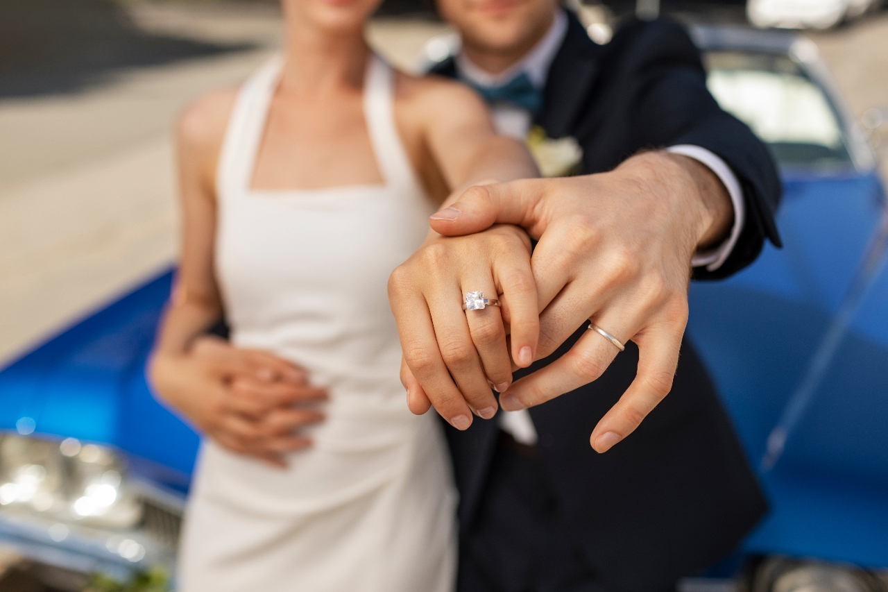 A close-up of a newlywed couple, showcasing a bride’s diamond engagement ring and a groom’s wedding band.