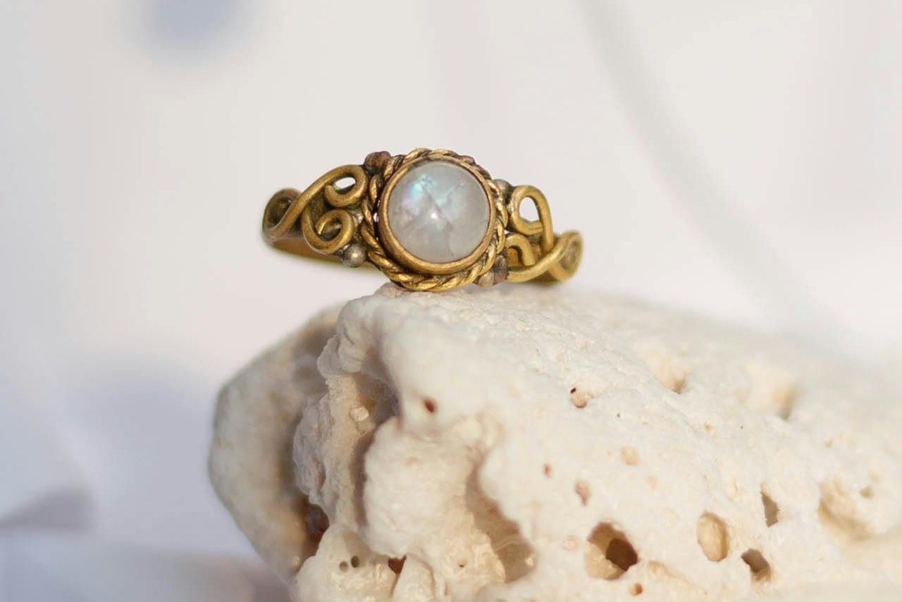 A vintage yellow gold ring with an opal gemstone sitting on a white rock.