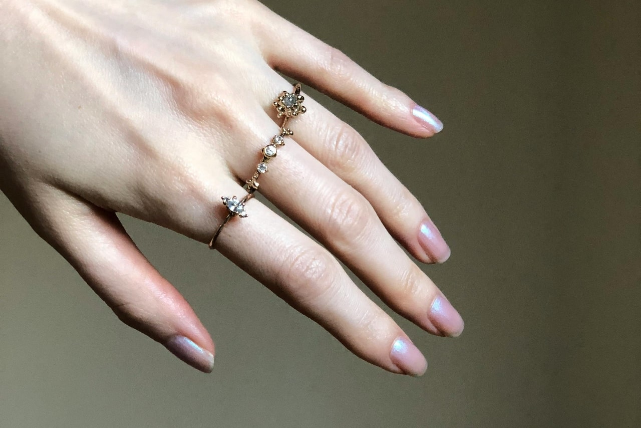 A manicured hand with three distinctive yellow gold rings on the index, middle, and ring finger.
