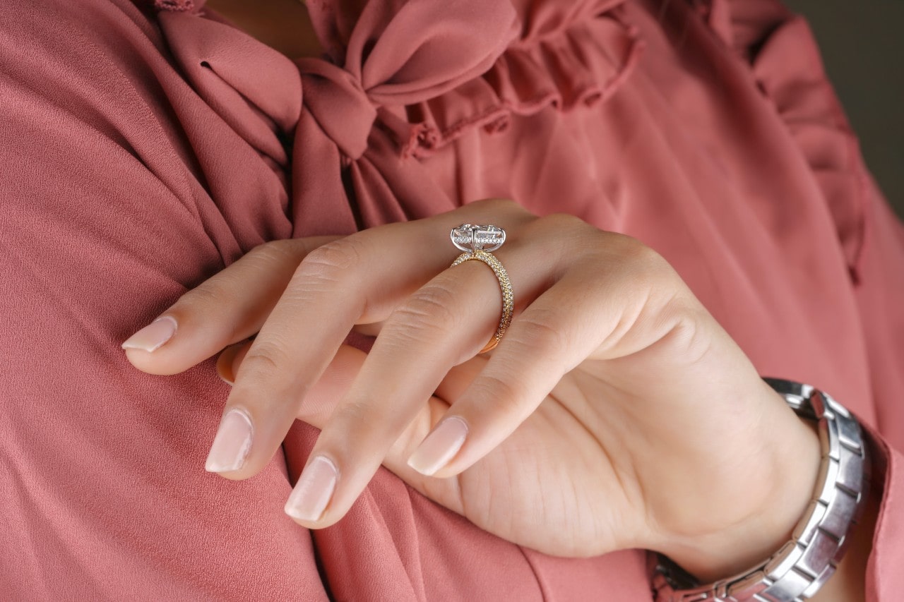 a woman holding her hand wearing a gold engagement ring against her pink blouse