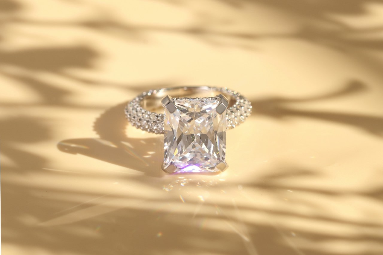 a glittering radiant cut engagement ring with sidestones on a beige surface