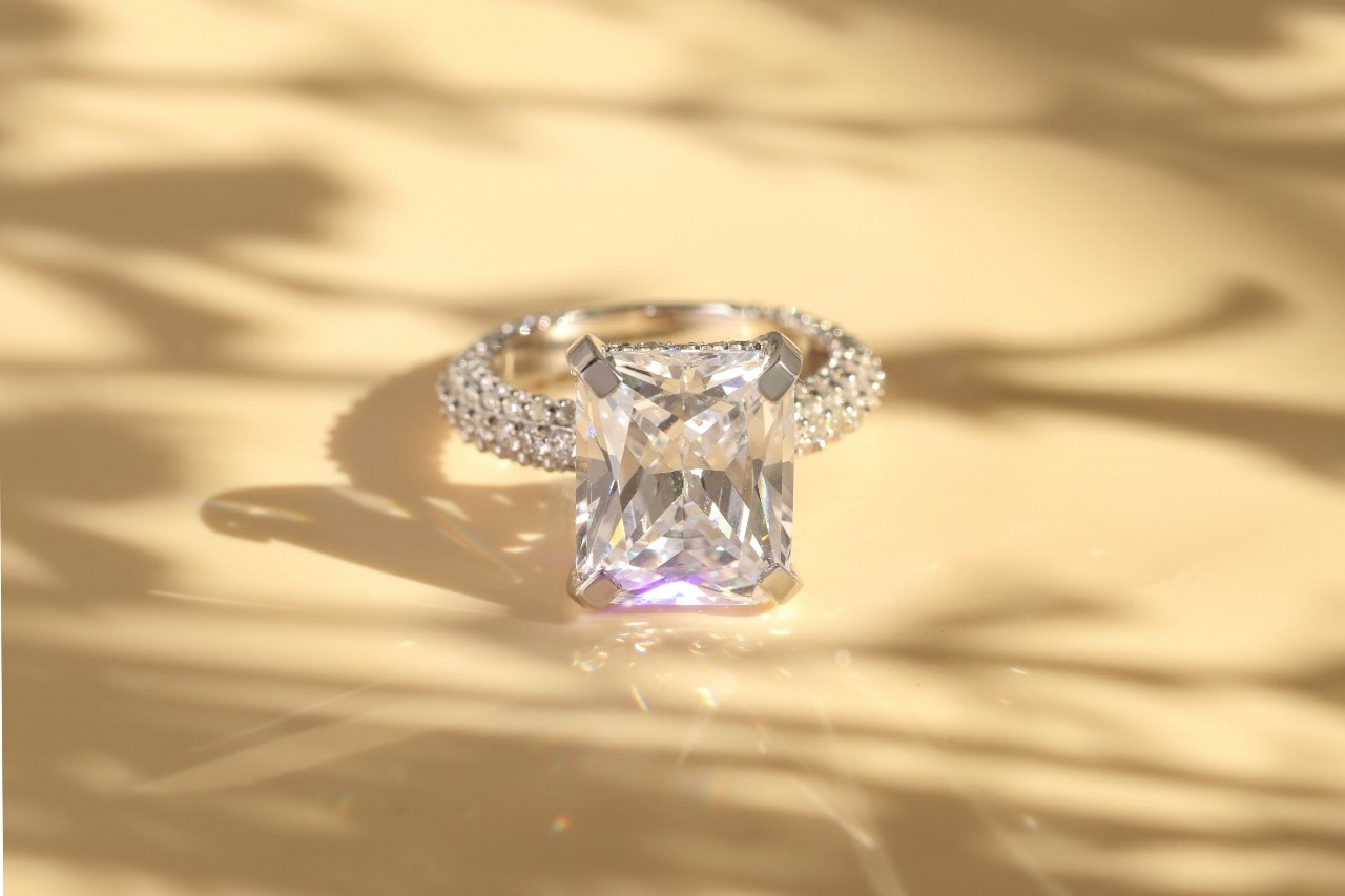 a glittering radiant cut engagement ring with sidestones on a beige surface a glittering radiant cut engagement ring with sidestones on a beige surface
