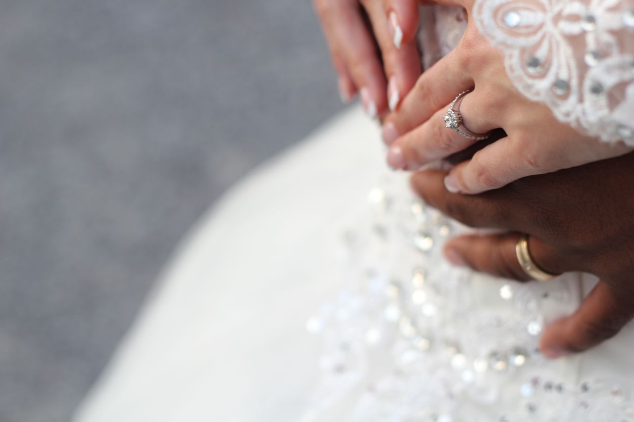 A close up of a bride’s round cut diamond engagement ring as she rest her hands on her groom’s. 