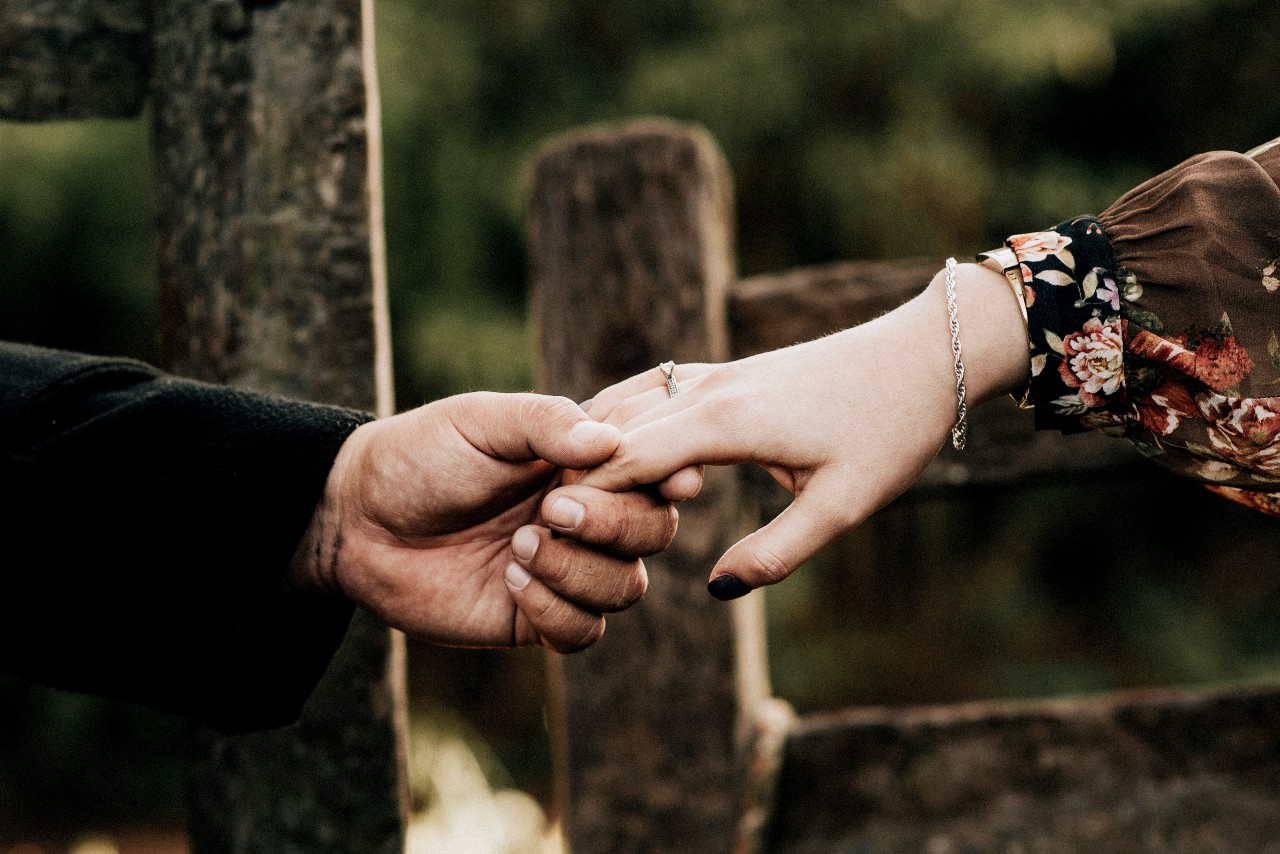 A closeup of a woman’s hand with a bracelet and engagement ring holding a man’s hand.