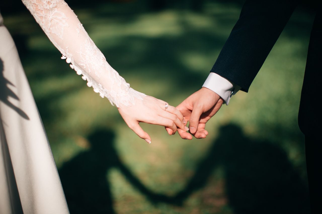 A close-up of a couple holding hands, with a focus on the bride's gorgeous wedding band.