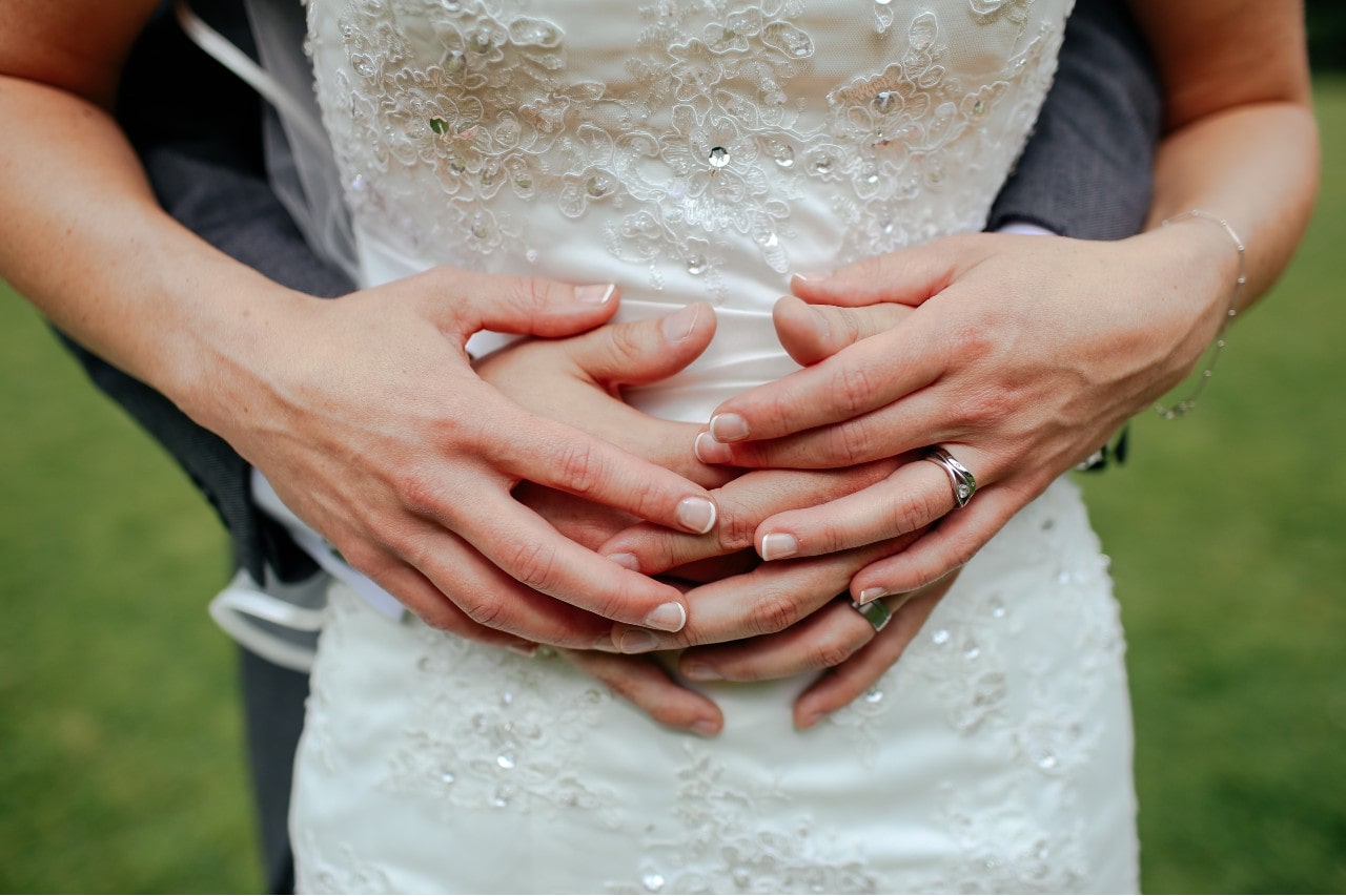 A close-up of a couple's hands embracing, showcasing exquisite wedding bands with a focus on a bride's intricate lace wedding dress.