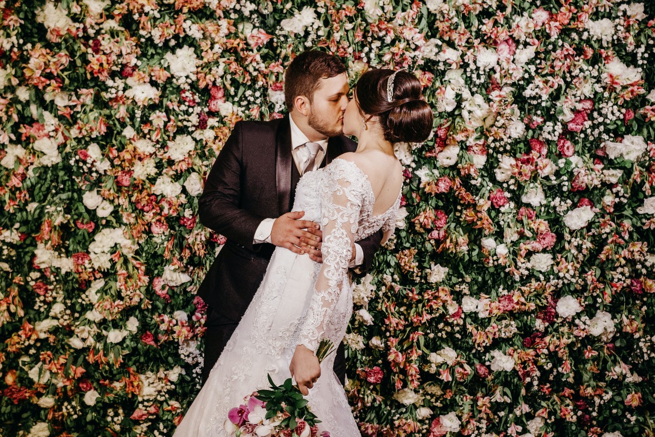 A bride and groom kiss in front of a flower wall.
