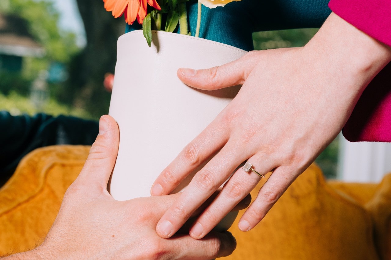 a couple passing a flower pot – the woman wearing a solitaire gemstone engagement ring