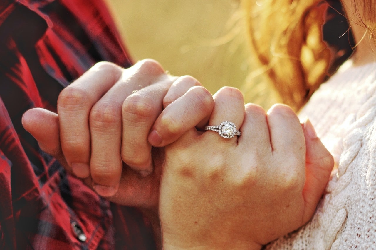 a couple intertwining pinkies – the woman wearing a halo engagement ring