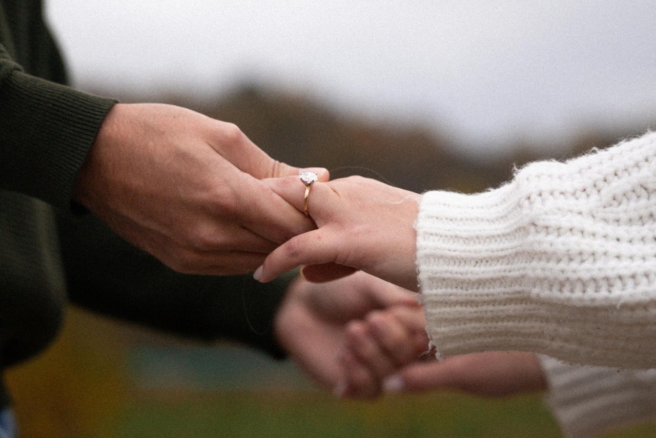 Close up of a couple holding hands with a strong emphasis on a yellow gold diamond engagement ring.