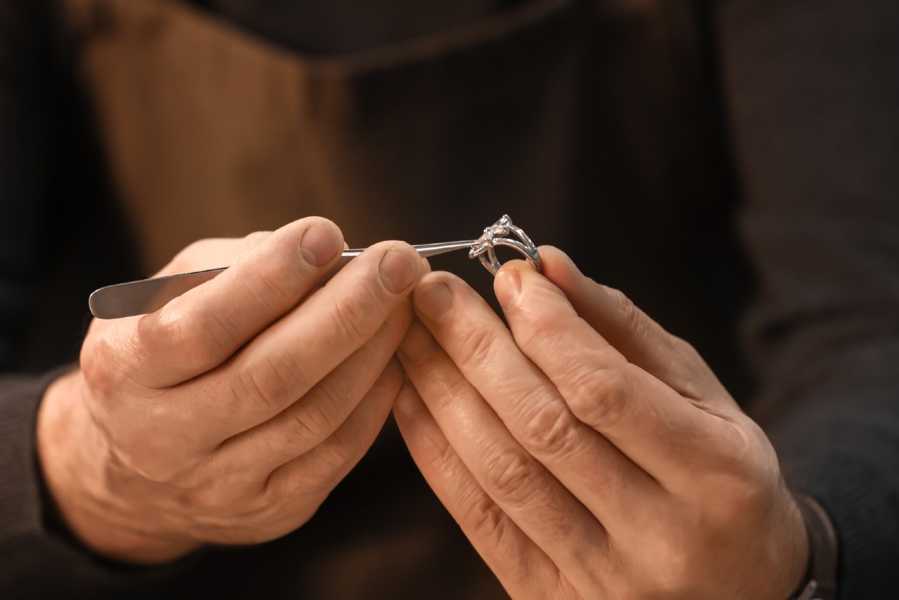 A jeweler carefully inspects and adjusts a silver ring with a gemstone using precision tools.