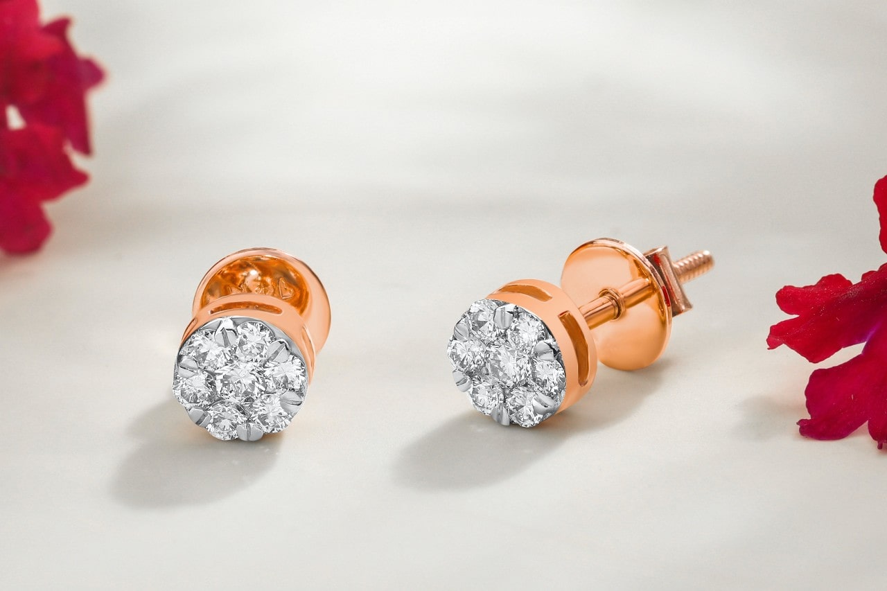 a pair of rose gold and diamond stud earrings on a white surface surrounded by red flowers