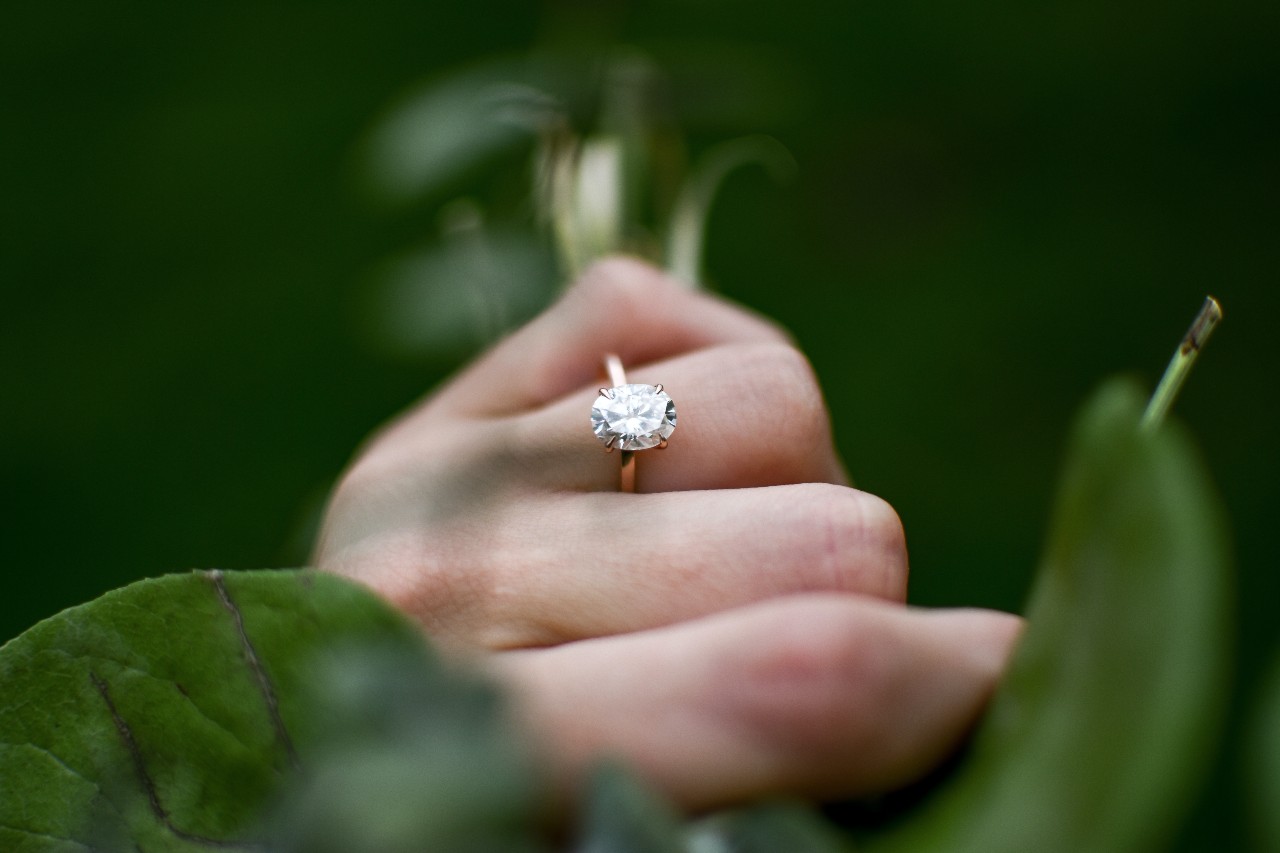 a woman’s hand holding a bunch of stems and wearing a solitaire engagement ring