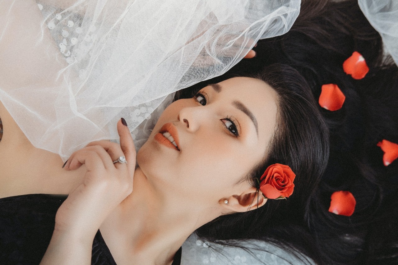 a woman lying down with roses in her hair wearing an engagement ring