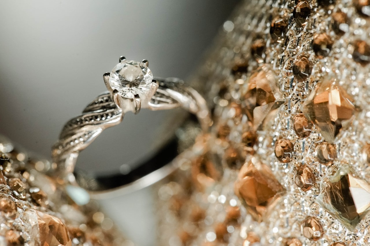 close up image of a diamond engagement ring and gemstone studded fabric