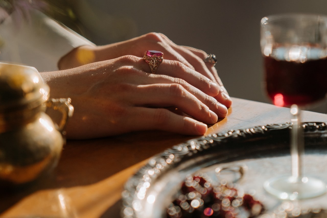 a woman’s hands resting on a lavishly set table, wearing two large gemstone rings