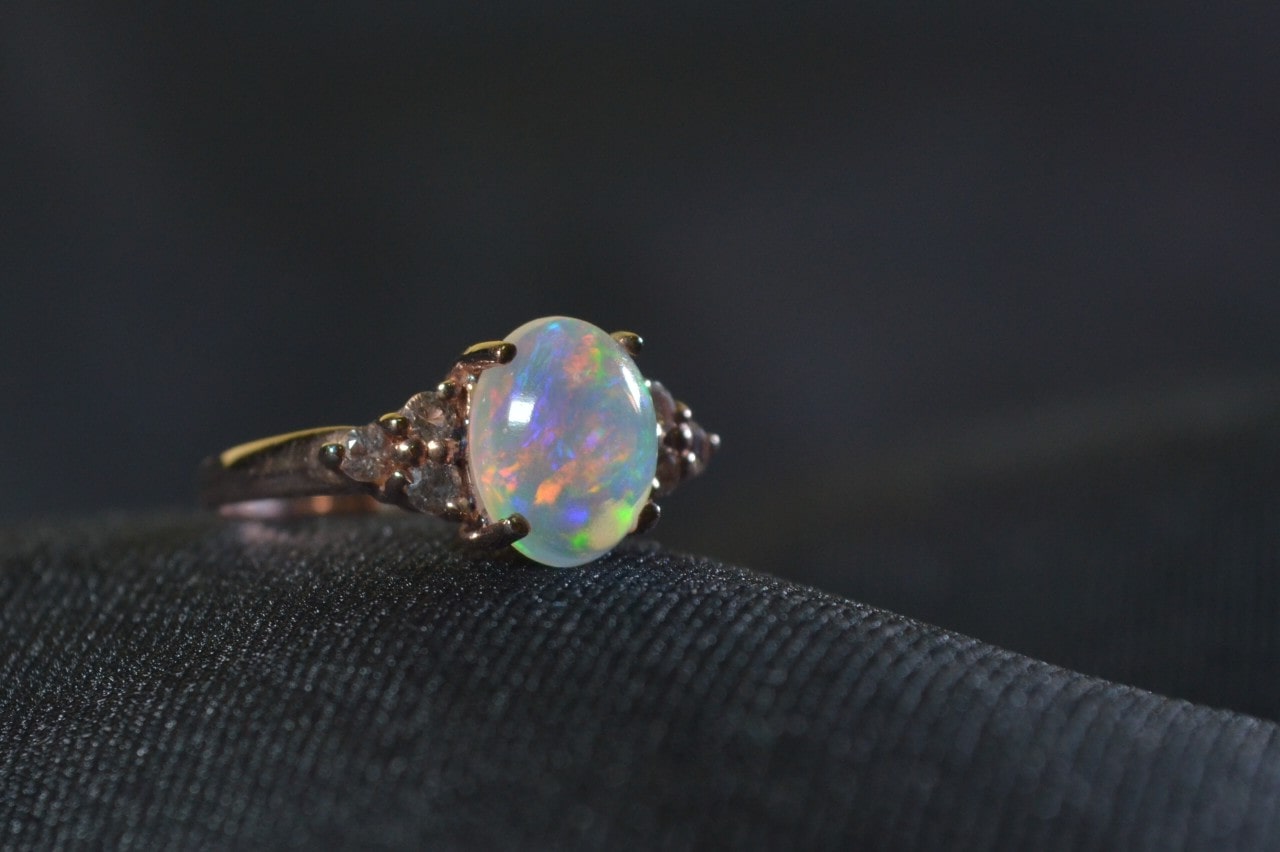 a white gold fashion ring featuring an oval cut opal on a textured black surface