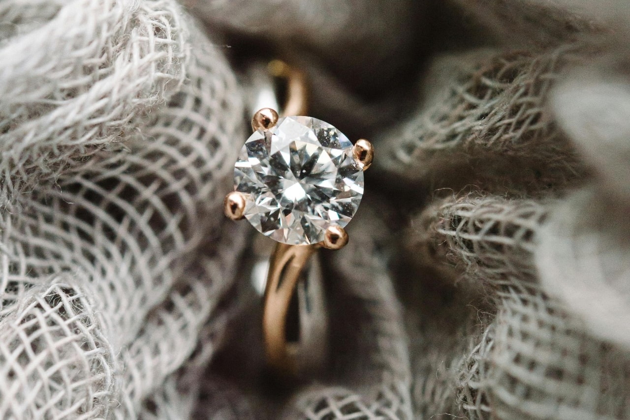A round-cut diamond yellow gold engagement ring is nestled in a textured grey fabric. A round-cut diamond yellow gold engagement ring is nestled in a textured grey fabric.